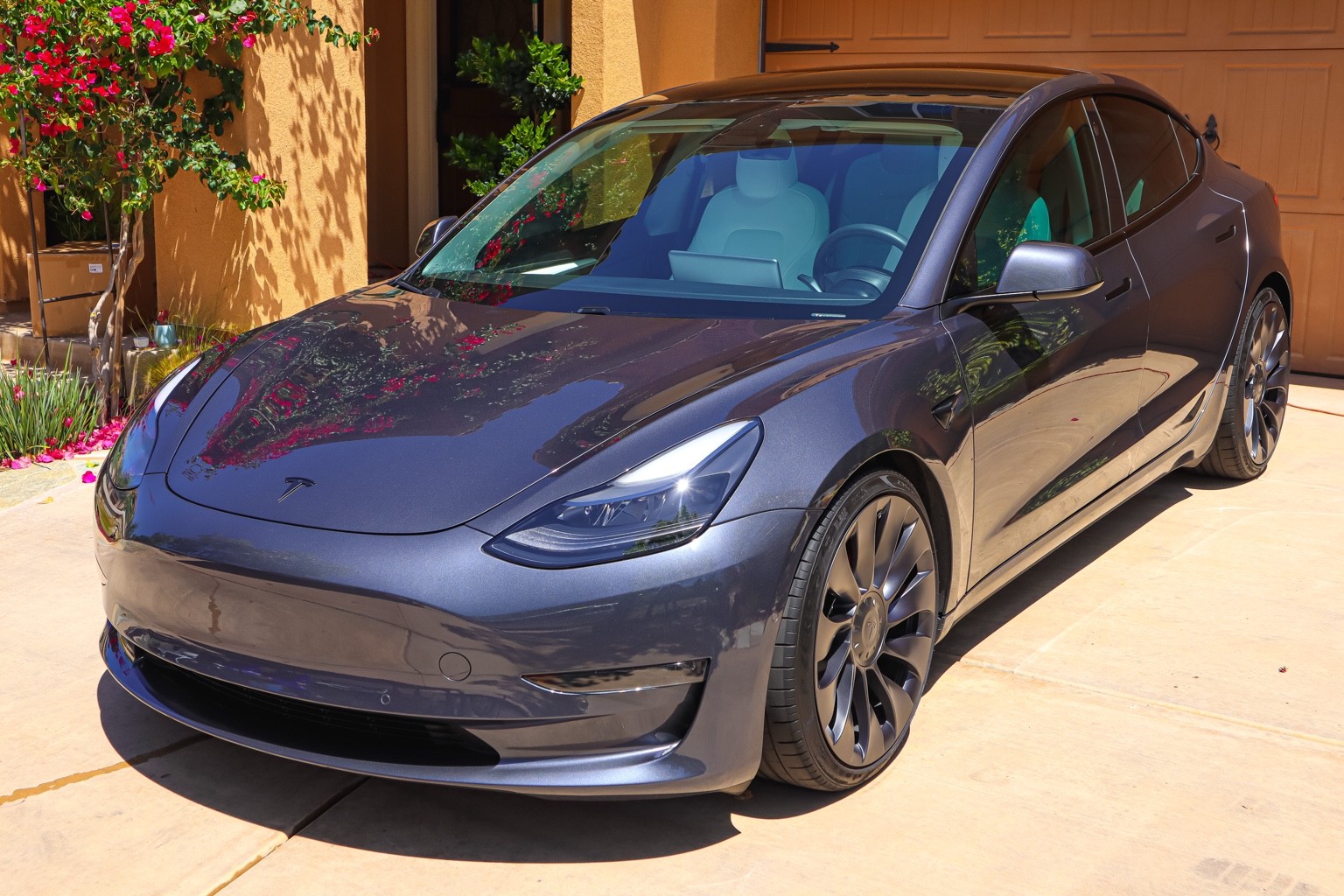 Glossy gray Tesla Model 3 in a sunlit driveway